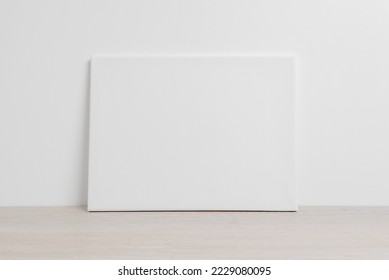 Art canvas in a horizontal position on the floor leaning against a white wall. Clean cloth for mockup art presentation