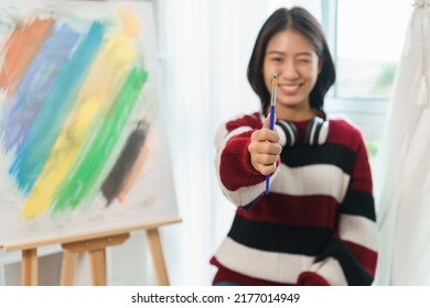 The art concept, Asian female artist doing measure proportion gesture with paintbrush in art studio.