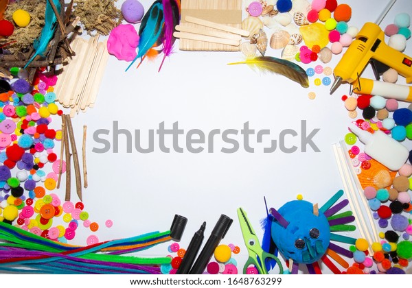 art and craft\
materials and tools - glue gun, scissors, pom-poms and popsicle\
sticks on white background