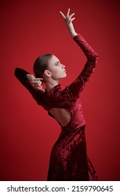 Art of dance, modern ballet. Beautiful ballet dancer girl in red velvet dress dances gracefully on a red background in the studio. 