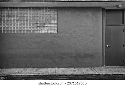 Art Deco Building With A Back Door.  Alleyway View Of An Old Building With Glass Block Window And Rear Doorway.  