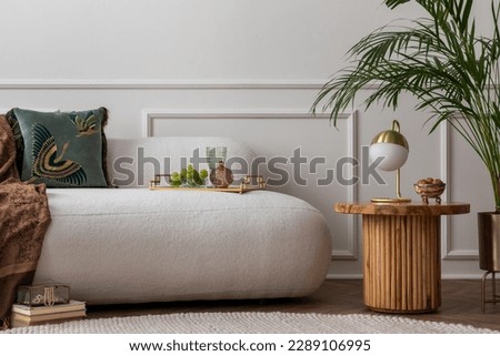 Art deco composition of living room interior with boucle sofa, plant, wooden coffee table, gold lamp, green pillow, elegant trace with glass, grape and personal accessories. Home decor. Template.