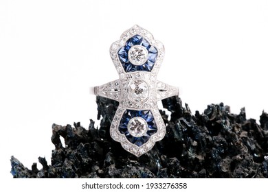 An Art Deco Style Sapphire And Diamond Ring On A Dark Black Rock With A White Background