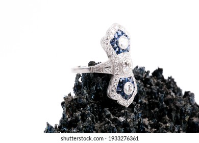 An Art Deco Style Sapphire And Diamond Ring On A Dark Black Rock With A White Background