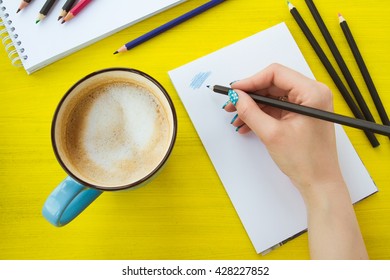 Art And Education Concept. Female Right Hand Holding Blue Pencil, Artist Making Sketch With Cup Of Coffee. Top View