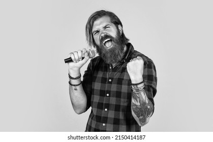 art. guy with beard singing in microphone. confidence and charisma on stage. bearded man wearing checkered shirt. rock music. male karaoke singer. mature charismatic male vocalist