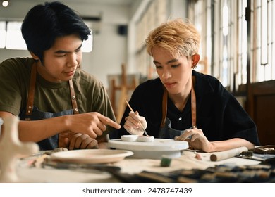 An art instructor guides an LGBT student as they paint a ceramic piece. Both are focused in a bright studio filled with pottery tools and materials, fostering a supportive learning environment. - Powered by Shutterstock