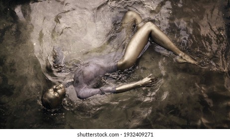 art performance of young graceful woman in water, covered by gold