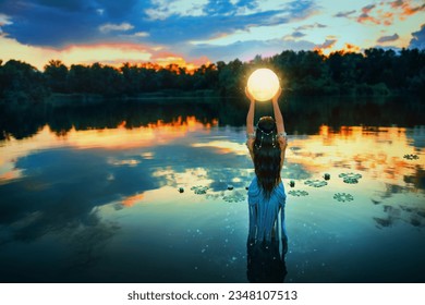 Art photo magic Fantasy woman and moon, holding universe planet in hands raises to dark night sky. Mystic witch Girl fairy elf river nymph stands in water lake summer nature. Lady queen back rear view