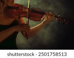 Art photo real person close-up lips, hand body part woman violinist cropped face musician plays music on the violin holding in hands musical instrument. Girl in black studio full smoke light dark room