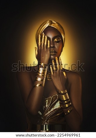 Art Portrait closeup Beauty fantasy african woman face in gold paint. Golden metallic shiny skin hand. Fashion model girl. Arab turban. Professional glamour makeup Gold jewellery, jewelry, accessories