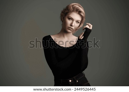 Art portrait of a graceful young blonde woman with a short haircut, posing expressively in black bodysuit. Dark gray studio background. Psychology. Female beauty.