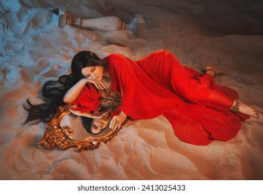 art Portrait real Fantasy girl arabic woman Fairy queen looks at reflection in mirror magic. beauty girl Lies in room full sand desert uae dubai. red long dress dream face fairy style night moon light