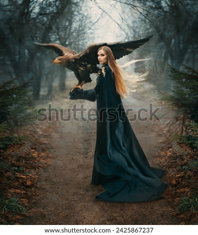 art portrait real people fantasy woman holding white-tailed eagle bird flaping open wings on hand. Elf blonde hair girl with brown bird walking in forest. Lady queen back, hunter black cape dark trees