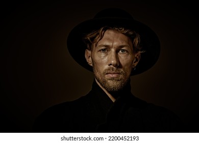 Art Portrait Of A Sad And Thoughtful Mature Man With Beard And Moustache Dressed In Black Coat And Black Hat Looking With Pain And Suffering At The Camera. Dark Key Portrait On A Black Background. 