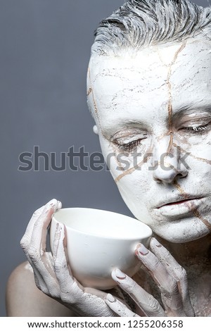 Art portrait of woman covered in clay holding white  cup.  Kintsugi  concept or facial therapy