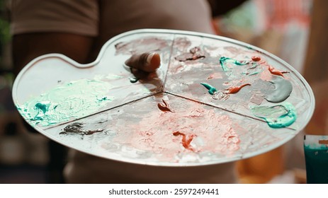 In an art studio, painter mixes multiple watercolor paints on a palette to create artwork on canvas. Skilled man painting with tools and showing imagination, artistic creation. Close up. Camera A.