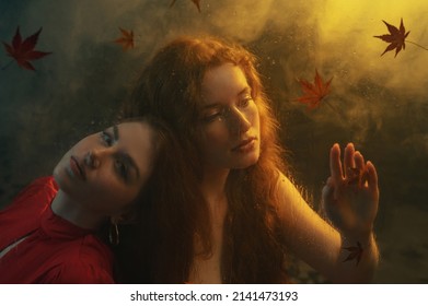 Art studio portrait made through the wet glass with red autumn leaves. Two beautiful redhead freckled women with long natural curly hair posing in smoke, darkness and warm light. Film grain effect
 - Powered by Shutterstock