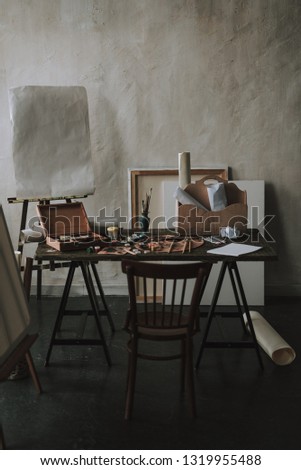 Art studio with table and painting equipment on it. Drawing easel on the background