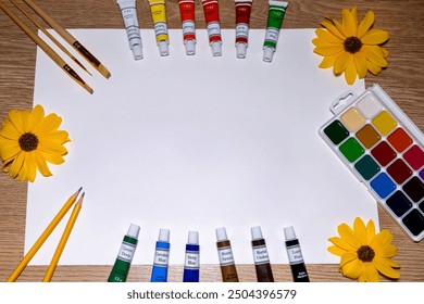 Art supplies arranged around blank paper with yellow flowers. A collection of art supplies, including paint tubes, watercolor palette, brushes, and pencils, neatly arranged around a blank sheet of - Powered by Shutterstock