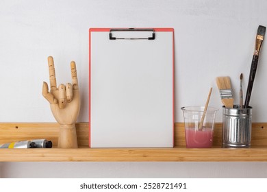 Art supplies on a shelf, paintbrushes, blank clipboard, and wooden hand model, art and craft mockup. Art supplies like paintbrushes and blank clipboard mockup, creative art and craft space - Powered by Shutterstock