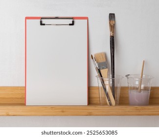 Art supplies on a wooden shelf: clipboard, paintbrushes, and cups. Clipboard and paintbrushes for art projects. Wooden shelf with art tools and supplies. - Powered by Shutterstock