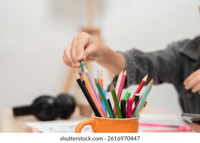 Art Supplies and Organization. A child selecting colored pencils from a container for drawing.