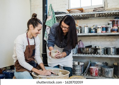 An art teacher giving instruction, help and tips to a student learning to throw clay on a pottery wheel during a lesson.  - Powered by Shutterstock