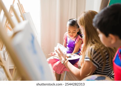 Art teacher guiding a young girl in selecting colors from a palette during an art class, fostering creativity and artistic expression - Powered by Shutterstock