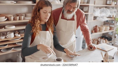 Art teacher, pottery and senior man in a class, learning tips in art class. Young woman teaching old man to roll clay, sculpture and giving instruction in studio to learn new skill in retirement - Powered by Shutterstock