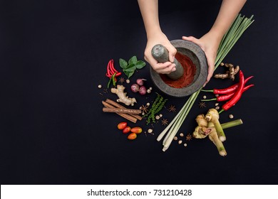 The Art of Thai Cuisine - Thai lady’s hands hold stone granite pestle with mortar and red curry paste ingredient together with tropical herbs and spices on classic dark background at top view angle. - Powered by Shutterstock