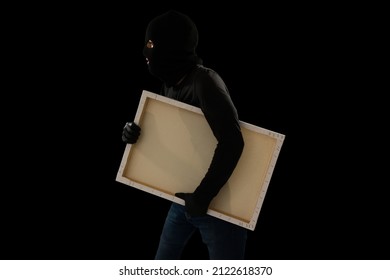 Art Theft. Dangerous Criminal With A Black Mask Stealing A Valuable Painting Against A Dark Background