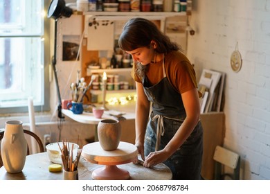 Art therapy for hobby or small business: young woman work in ceramics studio on handicraft jar production for handmade pottery shop. Artisan female shaping tableware from raw clay in workshop space