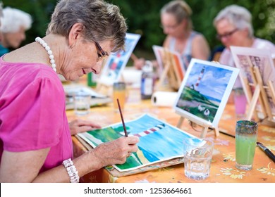 Art therapy for senior ladies, group of women painting the picture of lighthouse from the watercolor template  sitting at one table outdoors in the park. - Powered by Shutterstock