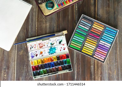 art workplace, pencils, brushes, watercolor paints, paper and crayon pastel chalks. Flat lay.wooden table - Powered by Shutterstock