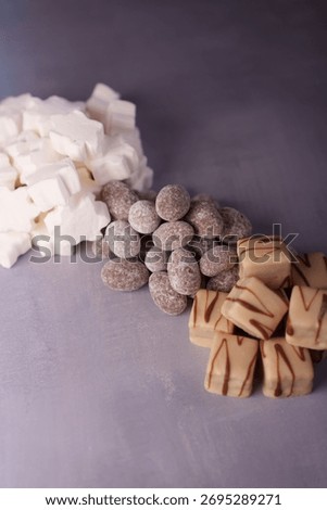 an artful display of assorted sweets: marshmallows, chocolate-coated almonds, and caramel drizzle chocolates on a subtle purple background, snowy, rectangular, displayed, gathered, stylized
