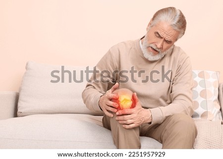 Arthritis symptoms. Senior man suffering from pain in his knee at home, space for text