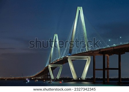 Arthur Ravenel Jr. Bridge, aka Cooper River Bridge, connects Charleston to Mount Pleasant and carries traffic on US-17. Photographed at night, with boats in the harbor.