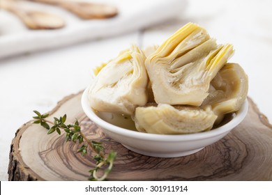 Artichoke hearts marinated in olive oil in a small white bowl on a white wooden background