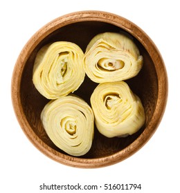 Artichoke hearts in wooden bowl over white. Cooked, canned flower buds of the globe artichoke, Cynara cardunculus var. scolymus, a thistle, cultivated as edible vegetable. Isolated macro food photo.