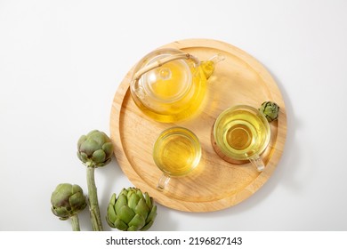 Artichokes Teapot In A Wooden Tray With Fresh Artichoke. Artichoke Tea Has The Ability To Fight Cancer, Lower Cholesterol, Improve Sleep, And Eliminate Toxins In The Body. 
 