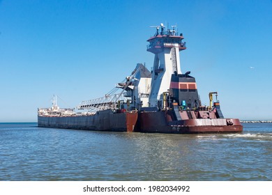 An articulated tugboat and barge bulk carrier leaving the Port of Cleveland, Ohio on Lake Erie.  Bright blue cloudless and sunny sky.