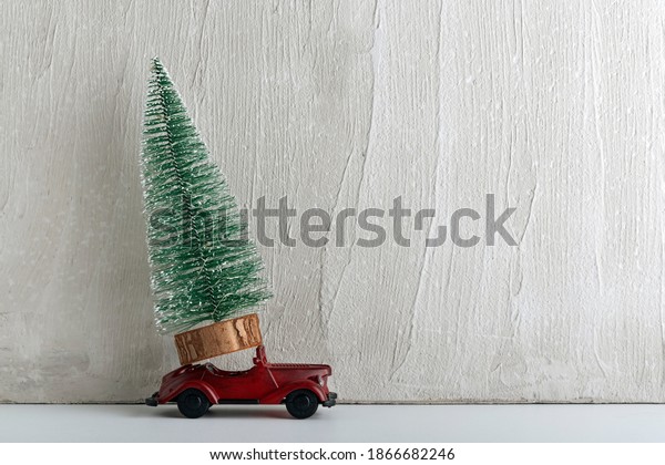 Artificial Christmas tree stands on small toy car.\
Delivery of trees. Car as\
gift.