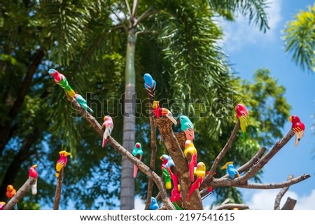 Artificial colorful parrot birds decorated on tree with blur green leaf against blue sky in park at summer.