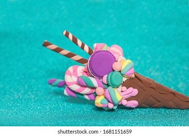 artificial dessert made of polymer clay. On a turquoise shimmering background. Ice cream in a waffle cone with marshmallows and macaroni.