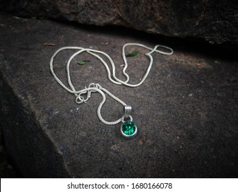 Artificial Emerald gemstone pendant with silver chain and stone background