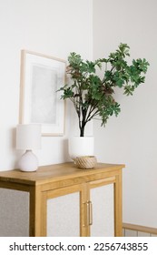 An artificial flower in a pot on a wooden chest of drawers in the living room, decorative items and a frame on the wall in a Scandinavian minimalist style - Shutterstock ID 2256743855