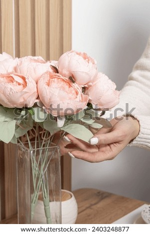 Artificial flowers for the interior. Bouquet of pink peonies in a glass vase. Woman adjusts flowers