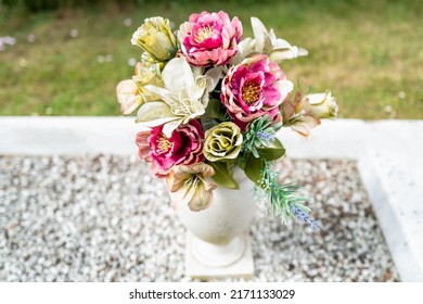 Artificial flowers seen in a porcelain vase located on a grave in a rural cemetery.