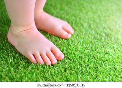 Artificial grass background. Tender foots of a baby on a green artificial turf floor.